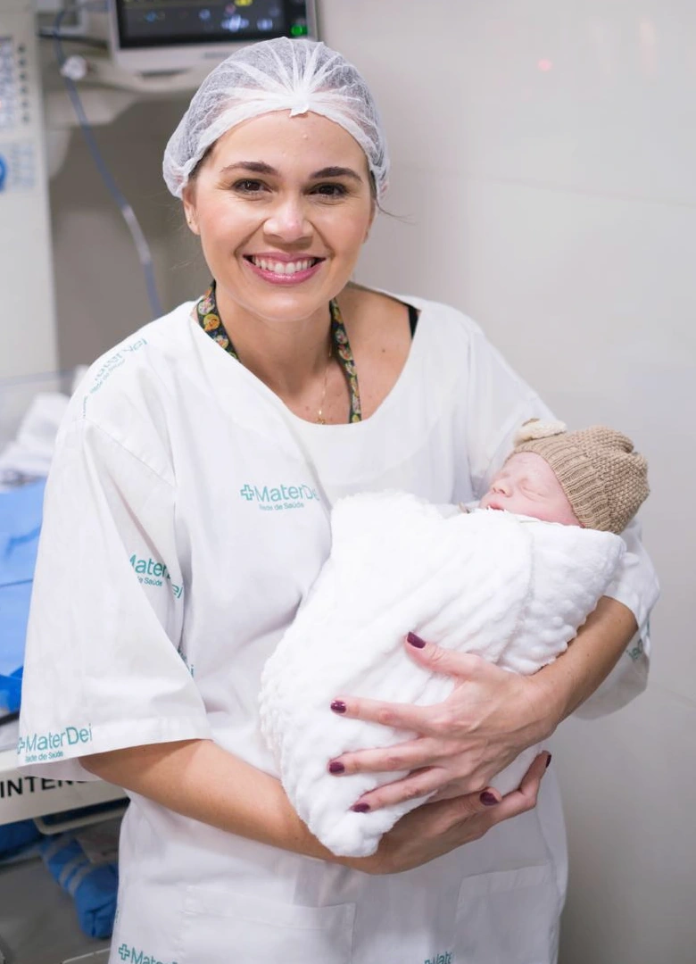 Dra. Amanda Soares sorrindo com um recém-nascido acolhido nos braços